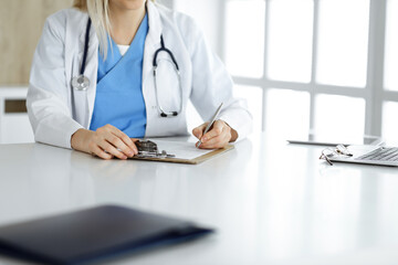 Unknown woman-doctor at work filling up medication history record form in clinic, close-up of clipboard