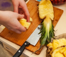 Cut pineapple close-up on the background of a knife, cutting Board and human hands separating the slices