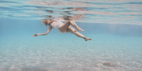 Woman in white swimsuit swims underwater in the crystal clear water of the tropical sea