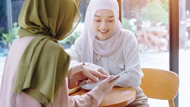 Young beautiful Asian Muslim women enjoying a relaxing moment working and playing with mobile phone in the coffee shop on a bright sunny day
