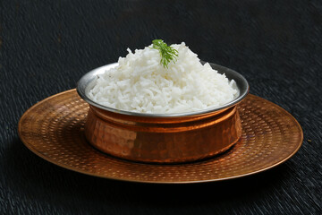 boiled white rice served in bronze metal bowl and plate black background