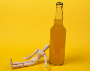 Alcoholism. Wooden puppet and bottle of beer on yellow background.