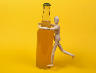 Alcoholism. Wooden puppet and bottle of beer on yellow background.
