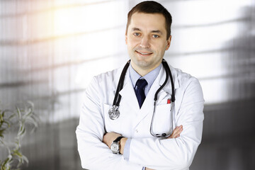 Professional doctor with a stethoscope is standing straight with crossed arms in a sunny clinic. Perfect medical service in a hospital. Best healthcare concept