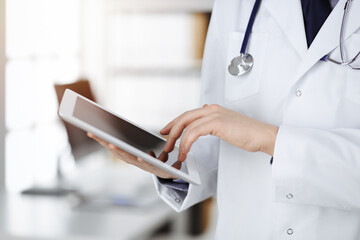 Unknown male doctor using tablet computer in sunny clinic, closeup. Perfect medical service in hospital. Medicine and healthcare concept