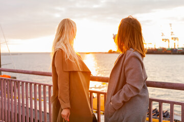 Two attractive women girlfriends in autumn coats at sunrise at the sea