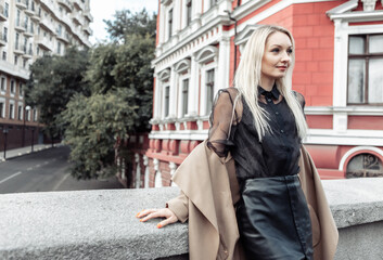 Cute attractive fashion woman in autumn coat posing against the background of urban architecture. Street fashion