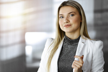 Young blonde business woman or female student standing straight and posing at camera in sunny office