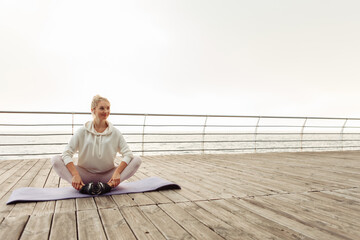 Young fitness woman resting while sitting on a mat on the beach. Healthy lifestyle concept