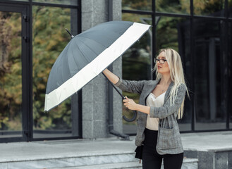 Blond business woman with umbrella on the background of a business office. Waiting for the rain