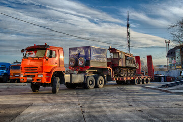 Fototapeta premium A large orange trawl truck with a semi-trailer and a tracked drilling rig loaded onto it. Epic HDR Shot
