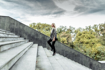 Purposeful, self-confident business lady climbs the stairs outdoors in cloudy weather. Career growth concept