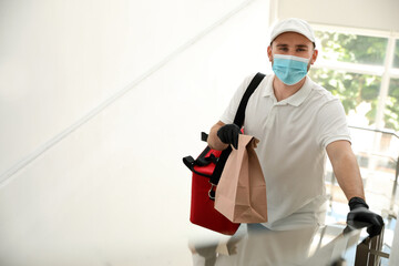 Courier in protective mask and gloves with order indoors. Restaurant delivery service during coronavirus quarantine