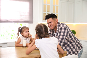 Little girls and their father eating together at table in modern kitchen