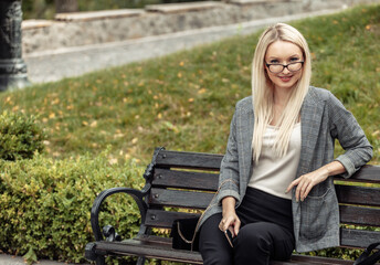 Naklejka na ściany i meble Blonde business lady sitting on a bench in the park