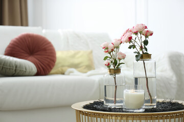 Burning candle and vases with beautiful roses on table indoors, space for text. Interior elements
