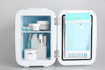 Open cosmetic refrigerator with skin care products on light background