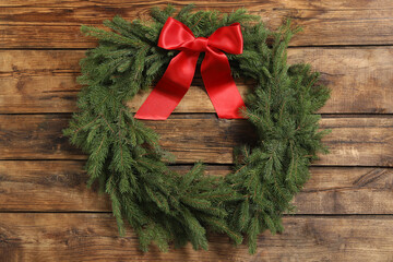 Christmas wreath made of fir branches with red bow on wooden background