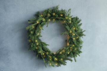 Beautiful Christmas wreath with festive lights on light blue wall © New Africa