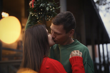 Fototapeta premium Happy couple kissing under mistletoe bunch outdoors