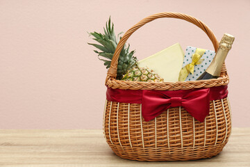 Fototapeta na wymiar Wicker gift basket with pineapple and bottle of champagne on wooden table. Space for text