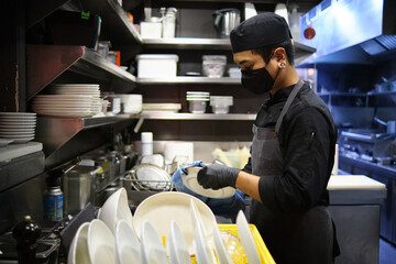Worker cleaning dishes at restaurant kitchen.