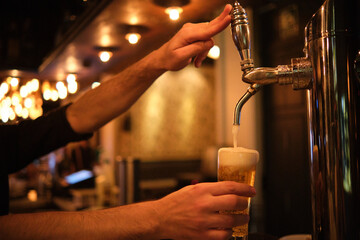 Barman pouring beer in glass from beer tap.
