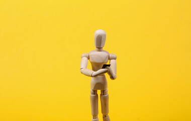 Wooden puppet uses smartphone on yellow background