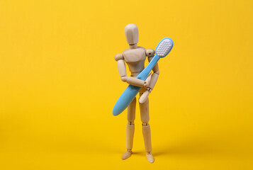 Wooden puppet holds a toothbrush on yellow background. Dental care