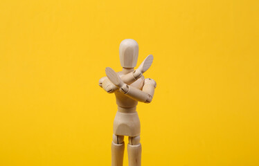 Wooden puppet crossed arms showing stop sign on yellow background