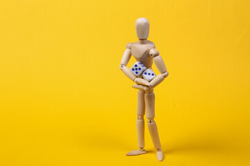 Wooden puppet holding dice on yellow background