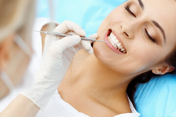 Young female patient visiting dentist office.Beautiful woman with healthy straight white teeth sitting at dental chair with open mouth during oral checkup while doctor working at teeth