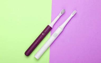 Two Modern electric toothbrushes on green pink pastel background. Top view. Teeth care. Minimalism