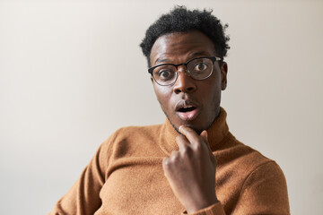 Genuine true human feelings, emotions and reactions. Isolated shot of funny emotional young black guy in eyeglasses gasping, opening mouth widely in disbelief, listening to incredible story