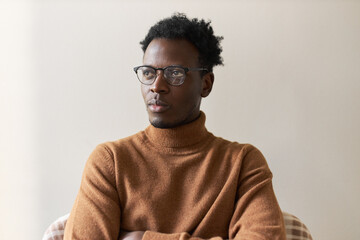 Job, occupation and career goals. Creative young Afro American male in turtleneck sweater and glasses posing isolated looking up with pensive facial expression, thinking about new start up project