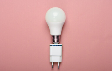 Smart energy-saving light bulb with a charger on pink background. Top view