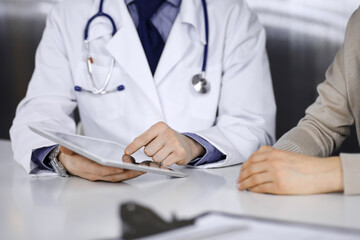 Unknown male doctor and patient woman discussing something while sitting in clinic and using tablet computer. Best medical service in hospital, medicine, pandemic stop