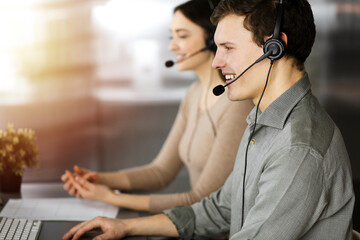 Call center operators at work. Two young people in headsets are talking to the clients, while sitting in sunny office