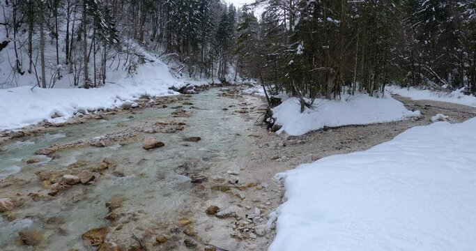 Colorful Sava Dolinka river flowing in Vrata valley, Slovenia. Alpine river flowing downstream in winter season. Snowy landscape. Tilt down, real time, wide angle