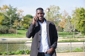 Young african black man speaking and smiling on the smartphone looking at camera in a park. Businessman on the phone.