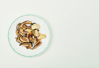 dried forest porcini mushrooms in a white saucer on a sheet of paper, free space for text.