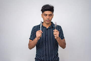 portrait of young boy looking into the fork and also holds a fork and a spoon against a white background.