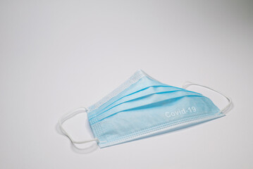 Covid-19 or coronavirus conceptual text on a blue mouth and nose surgical mask on light gray...