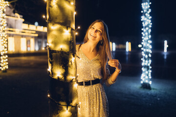 Junge Frau im Abendkleid posiert vor weihnachtlicher Parkbeleuchtung