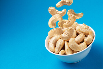 Falling cashew nuts into bowl on blue background, top view