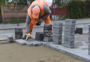A worker lays concrete tiles in even rows on the sand. Construction of a road for pedestrians.