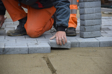 The builder settles the paving slabs in even rows, close-up. Construction of a road for pedestrians.