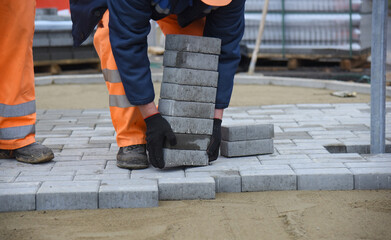 A worker lifts a lot of paving slabs, building a road for pedestrians.