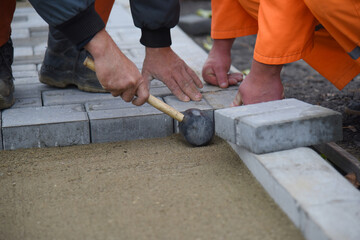 A worker lays new paving slabs, aligns it with a hammer. Construction of a road for pedestrians.