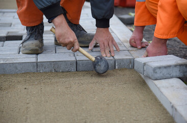A worker lays new paving slabs, aligns it with a hammer. Construction of a road for pedestrians.
